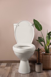 Photo of White toilet bowl and houseplant near beige wall indoors