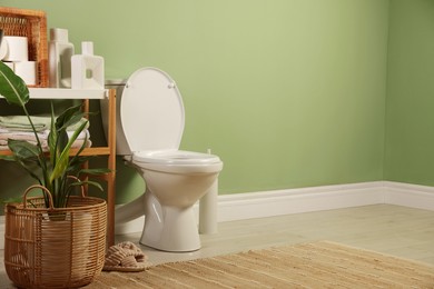 Photo of White toilet bowl, paper rolls, slippers and houseplants in bathroom, space for text