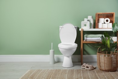 Photo of White toilet bowl, paper rolls, slippers and houseplants in bathroom, space for text