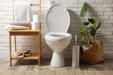 Photo of Ceramic toilet bowl and necessities near white brick wall in restroom