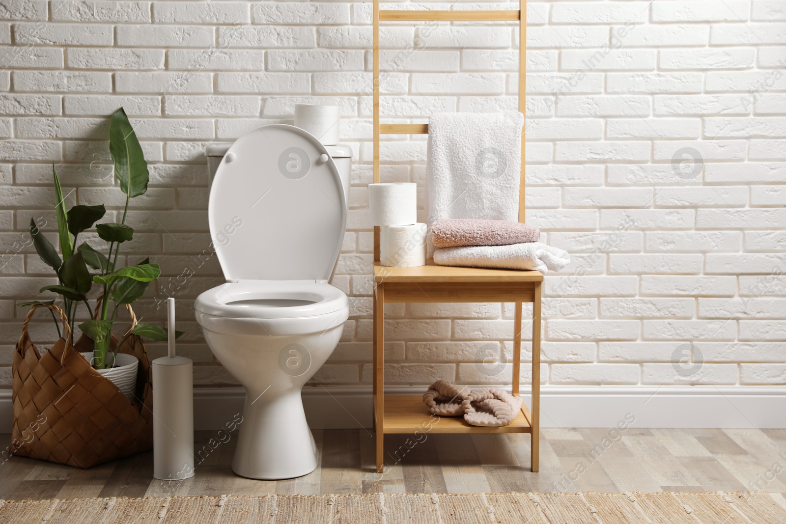 Photo of Ceramic toilet bowl and necessities near white brick wall in restroom