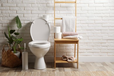 Photo of Ceramic toilet bowl and necessities near white brick wall in restroom