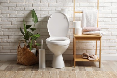 Photo of Ceramic toilet bowl and necessities near white brick wall in restroom