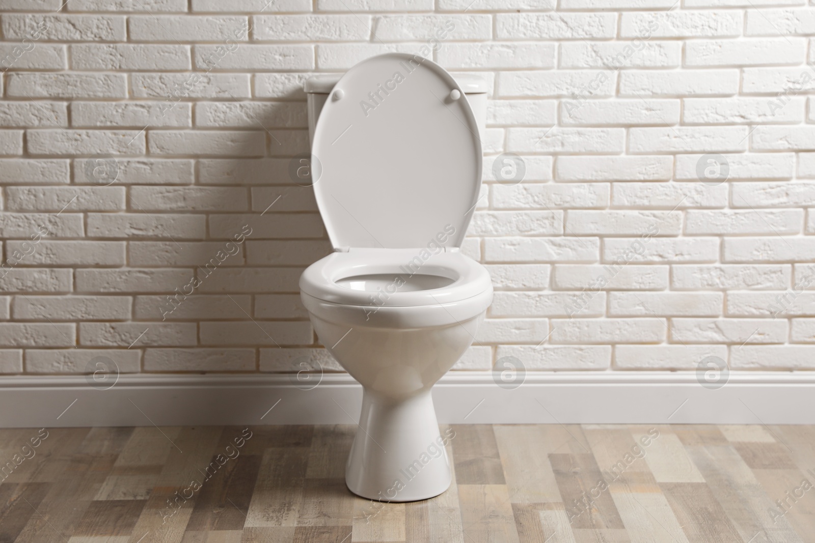 Photo of Ceramic toilet bowl near white brick wall in restroom