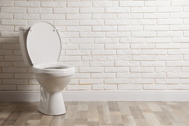 Photo of Ceramic toilet bowl near white brick wall in restroom. Space for text