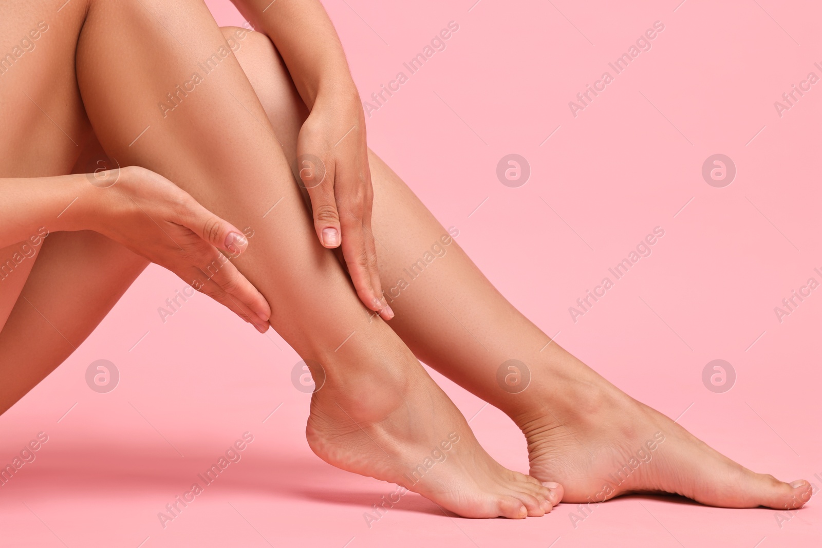 Photo of Woman touching her smooth legs on pink background, closeup