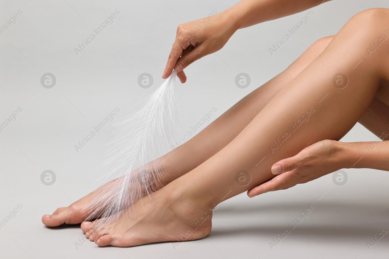 Photo of Woman with smooth legs and feather on grey background, closeup