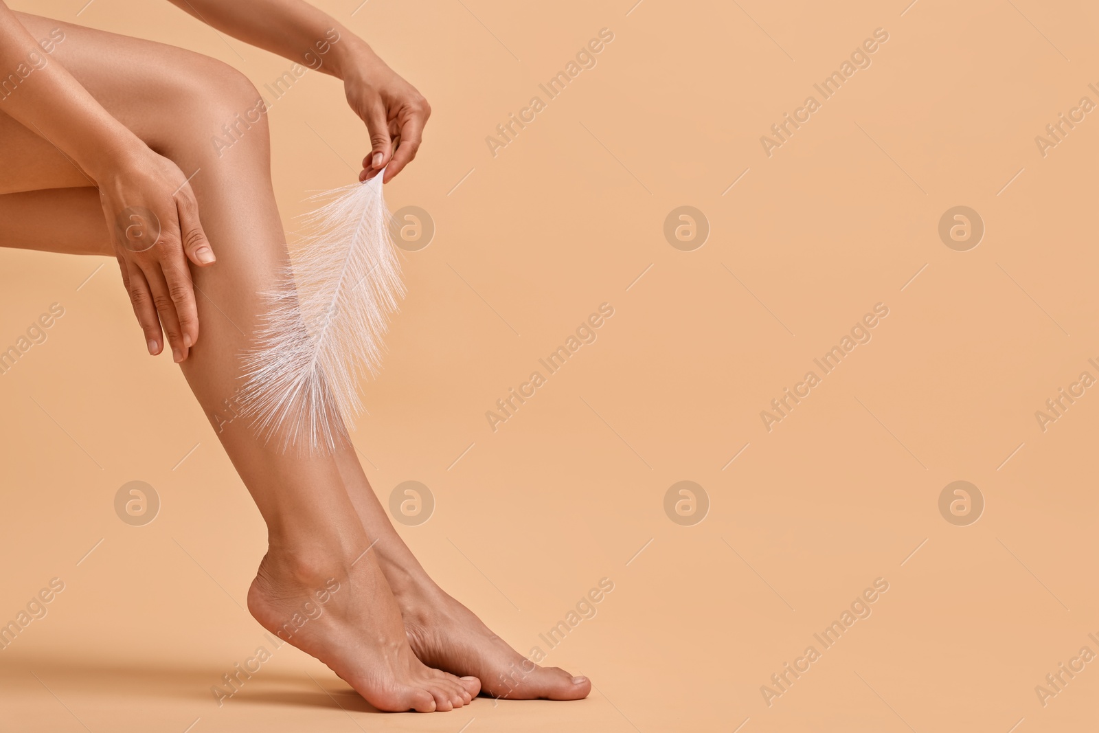 Photo of Woman with smooth legs and feather on beige background, closeup. Space for text