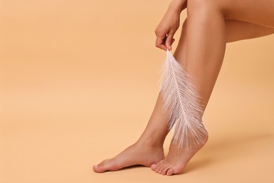 Photo of Woman with smooth legs and feather on beige background, closeup. Space for text