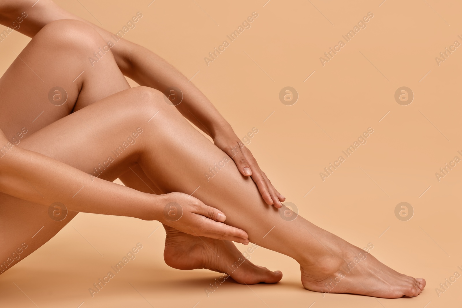 Photo of Woman touching her smooth legs on beige background, closeup