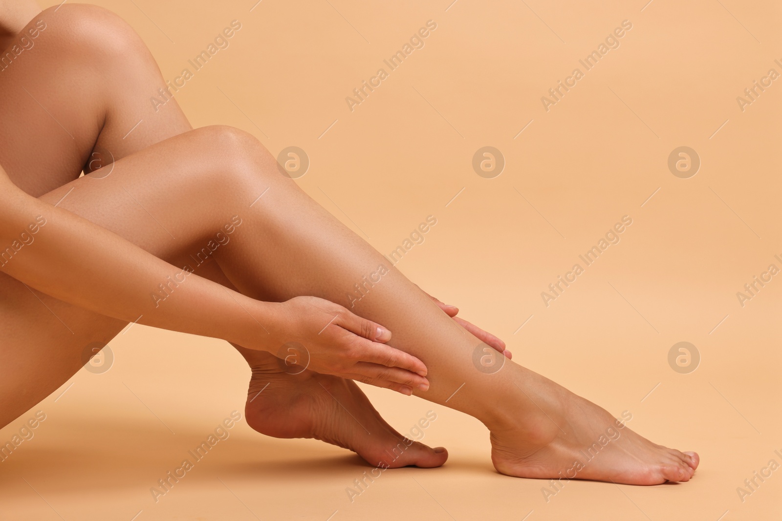 Photo of Woman touching her smooth legs on beige background, closeup