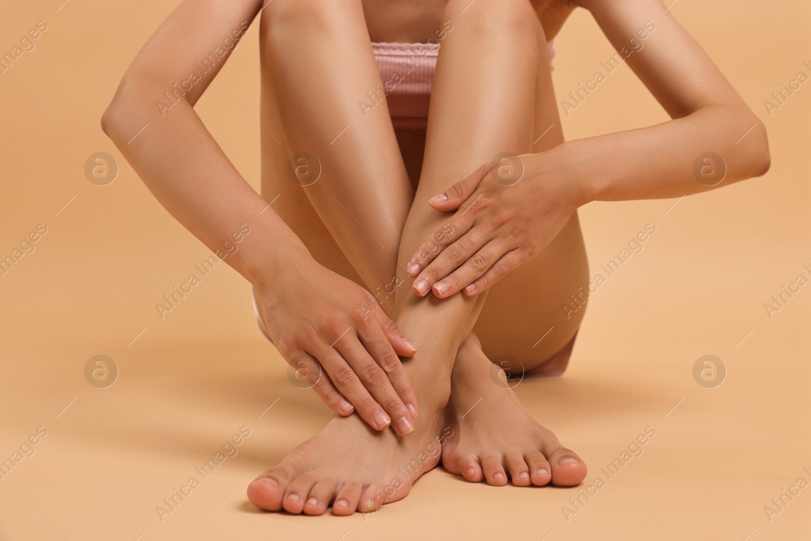 Photo of Woman touching her smooth feet on beige background, closeup