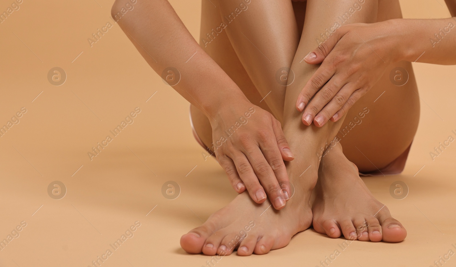 Photo of Woman touching her smooth feet on beige background, closeup