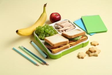 Photo of Lunch box with snacks and stationery on yellow table