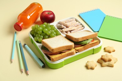 Photo of Lunch box with snacks, bottle of juice and stationery on yellow table