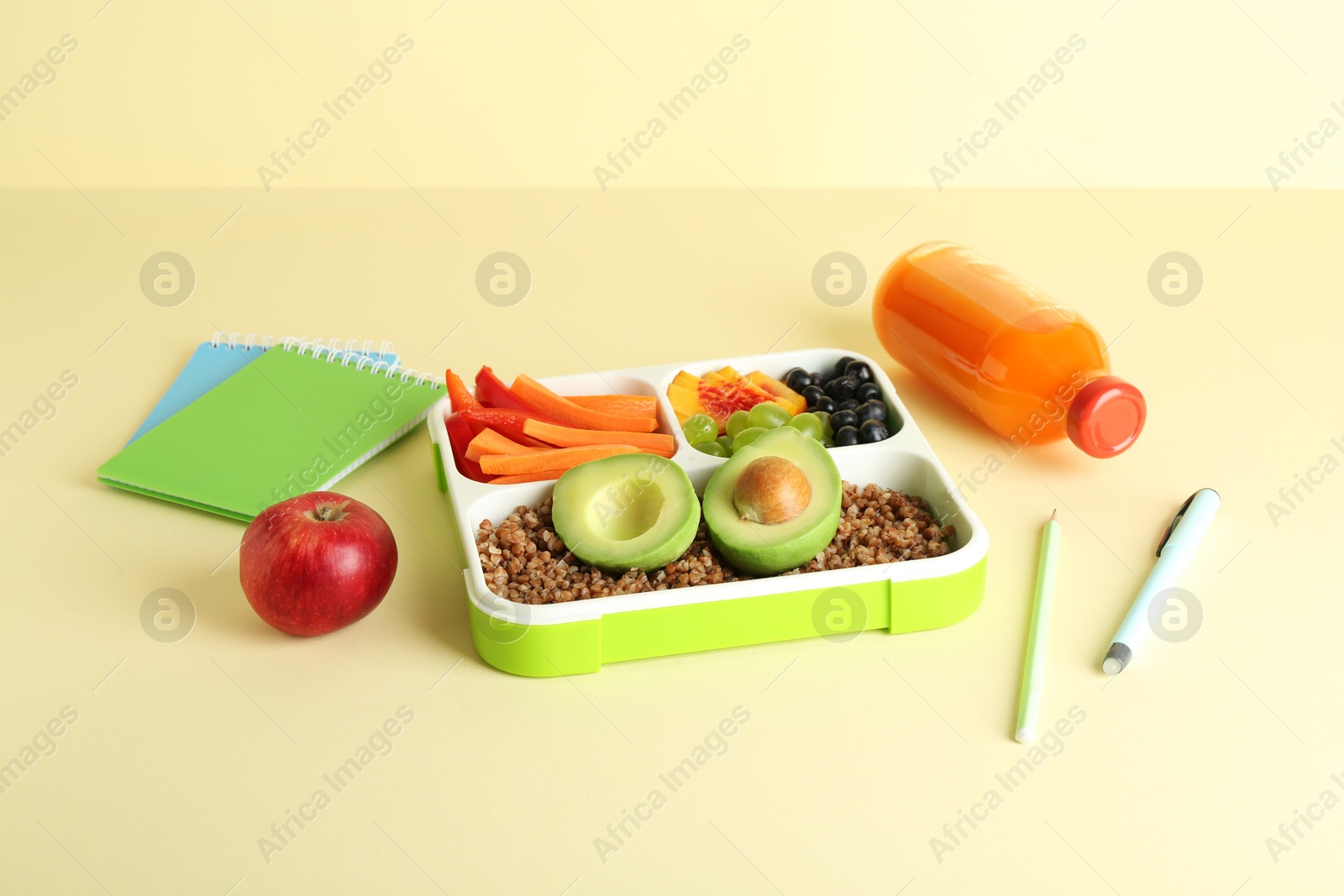 Photo of Lunch box with snacks, bottle of juice and stationery on yellow background