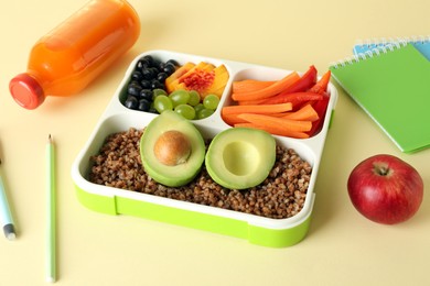 Photo of Lunch box with snacks, bottle of juice and stationery on yellow table