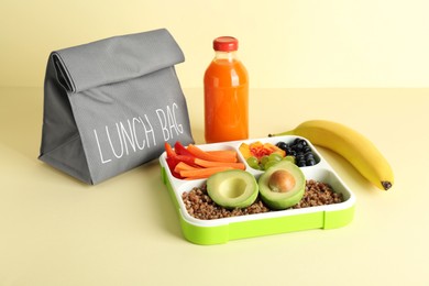 Gray bag, lunch box with snacks and bottle of juice on yellow background