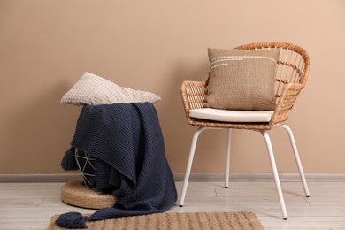 Soft pillows, wicker chair and blanket on floor near beige wall