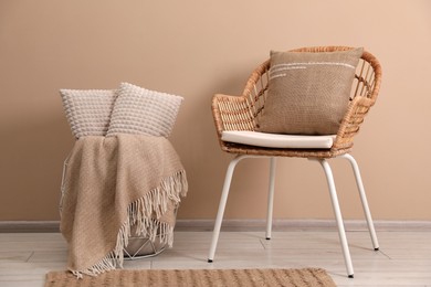 Photo of Soft pillows, wicker chair and blanket on floor near beige wall