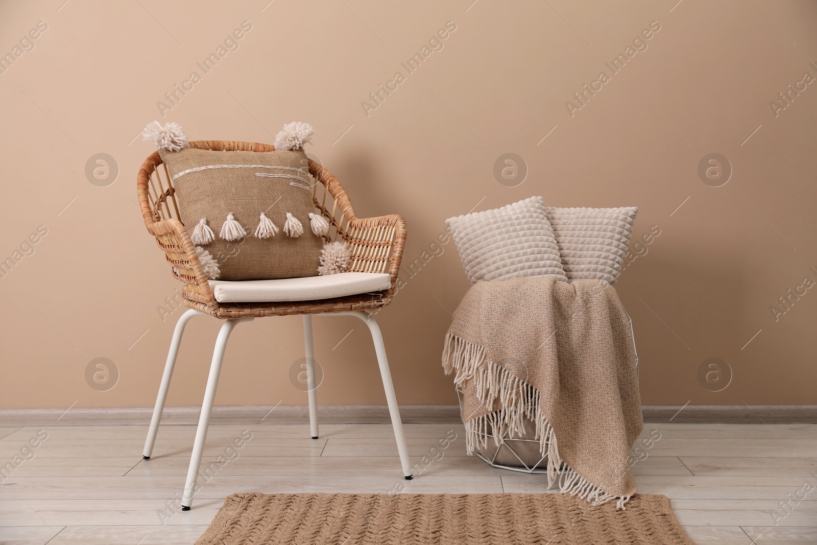 Photo of Soft pillows, wicker chair and blanket on floor near beige wall