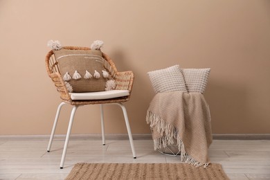 Soft pillows, wicker chair and blanket on floor near beige wall