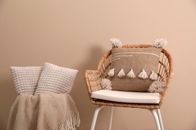 Photo of Soft pillows, wicker chair and blanket near beige wall