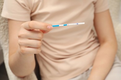 Woman holding negative pregnancy test indoors, closeup view