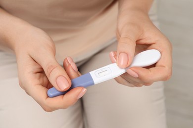 Photo of Woman holding pregnancy test indoors, closeup view