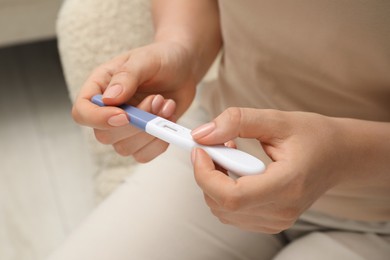 Photo of Woman holding pregnancy test indoors, closeup view