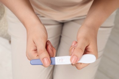 Photo of Woman holding positive pregnancy test indoors, closeup view