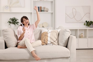 Happy young woman with pregnancy test on sofa at home