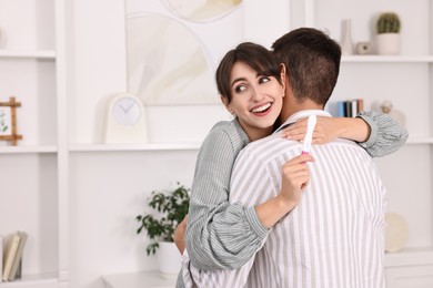 Happy young couple with pregnancy test at home, space for text