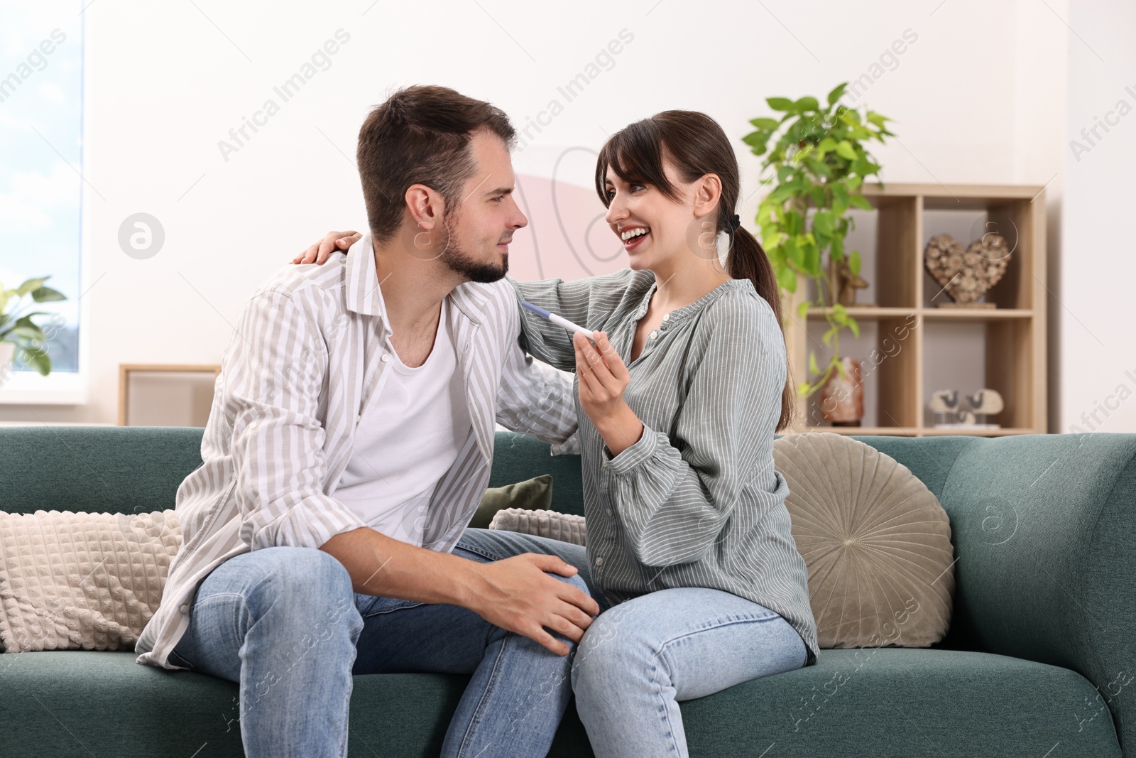 Photo of Happy young couple with pregnancy test on sofa at home