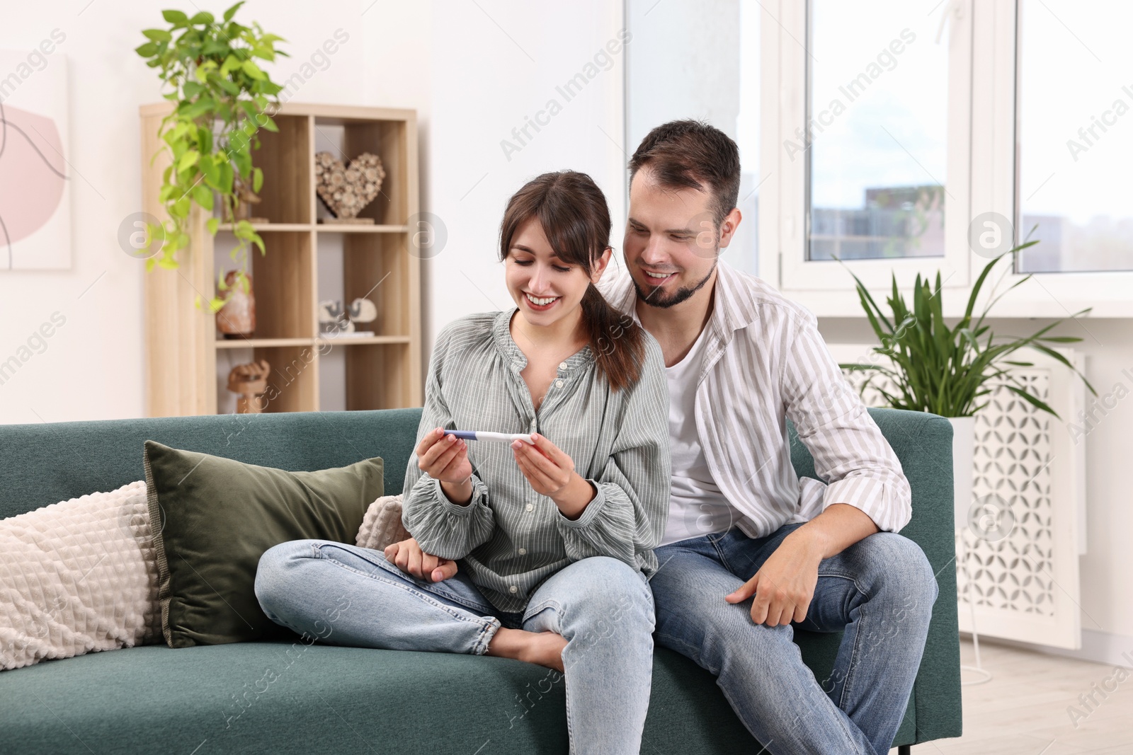 Photo of Happy young couple with pregnancy test on sofa at home