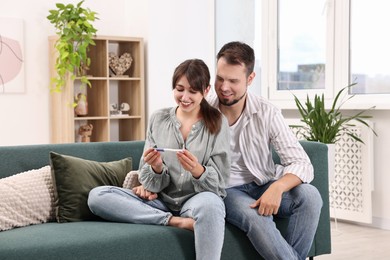 Photo of Happy young couple with pregnancy test on sofa at home