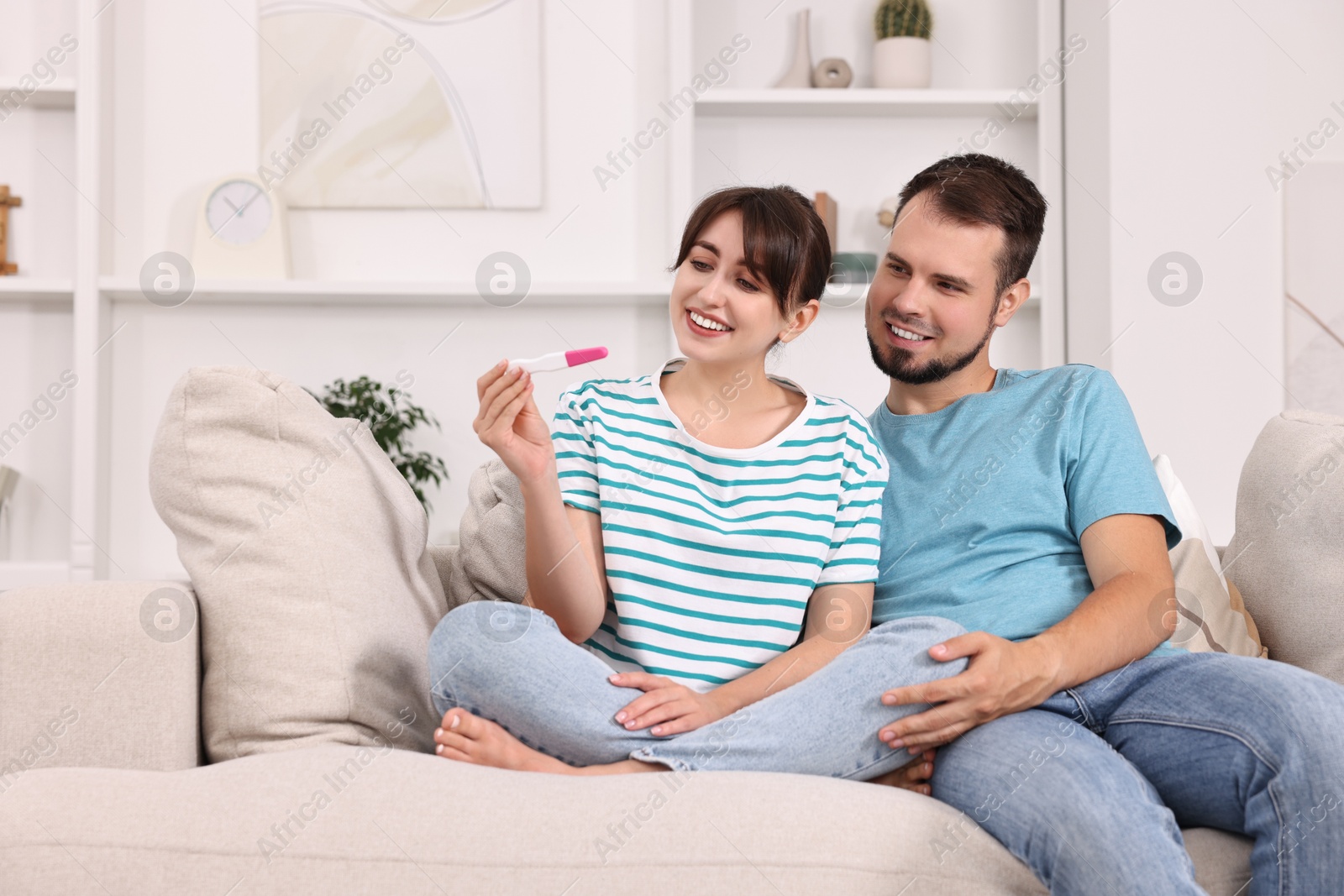 Photo of Happy young couple with pregnancy test on sofa at home