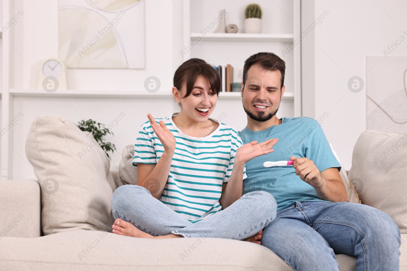 Photo of Happy young couple with pregnancy test on sofa at home