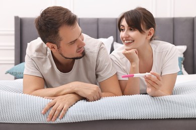 Photo of Happy young couple with pregnancy test on bed at home