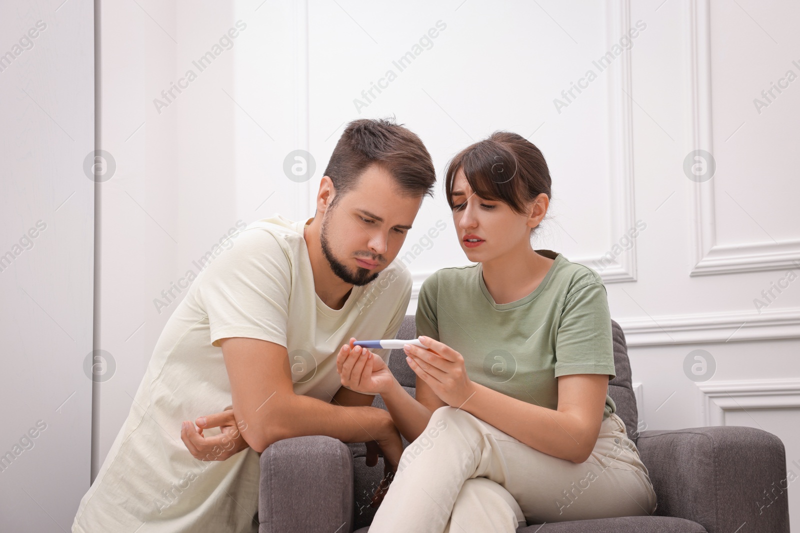 Photo of Worried young couple with pregnancy test at home