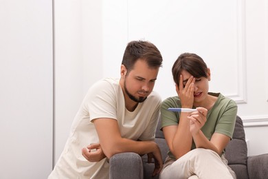 Photo of Worried young couple with pregnancy test at home