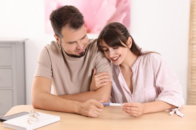 Happy young couple with pregnancy test at wooden table indoors