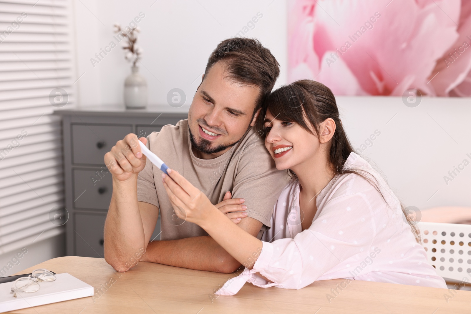 Photo of Happy young couple with pregnancy test at wooden table indoors