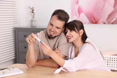 Happy young couple with pregnancy test at wooden table indoors