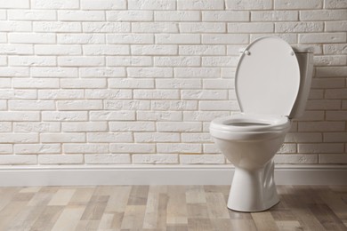 Photo of Ceramic toilet bowl near white brick wall in restroom. Space for text