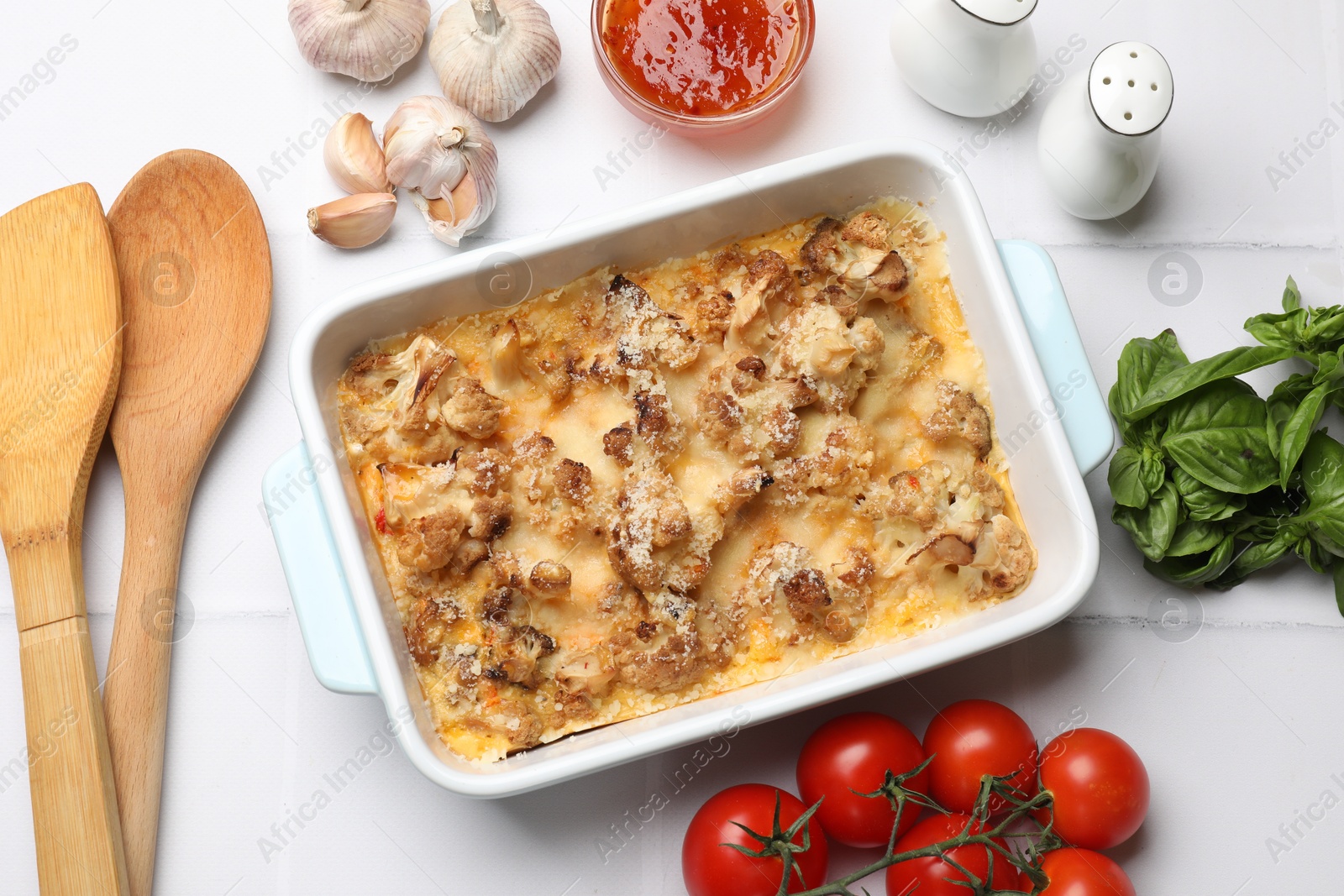 Photo of Tasty baked cauliflower, sauce, spices and products on white tiled table, flat lay