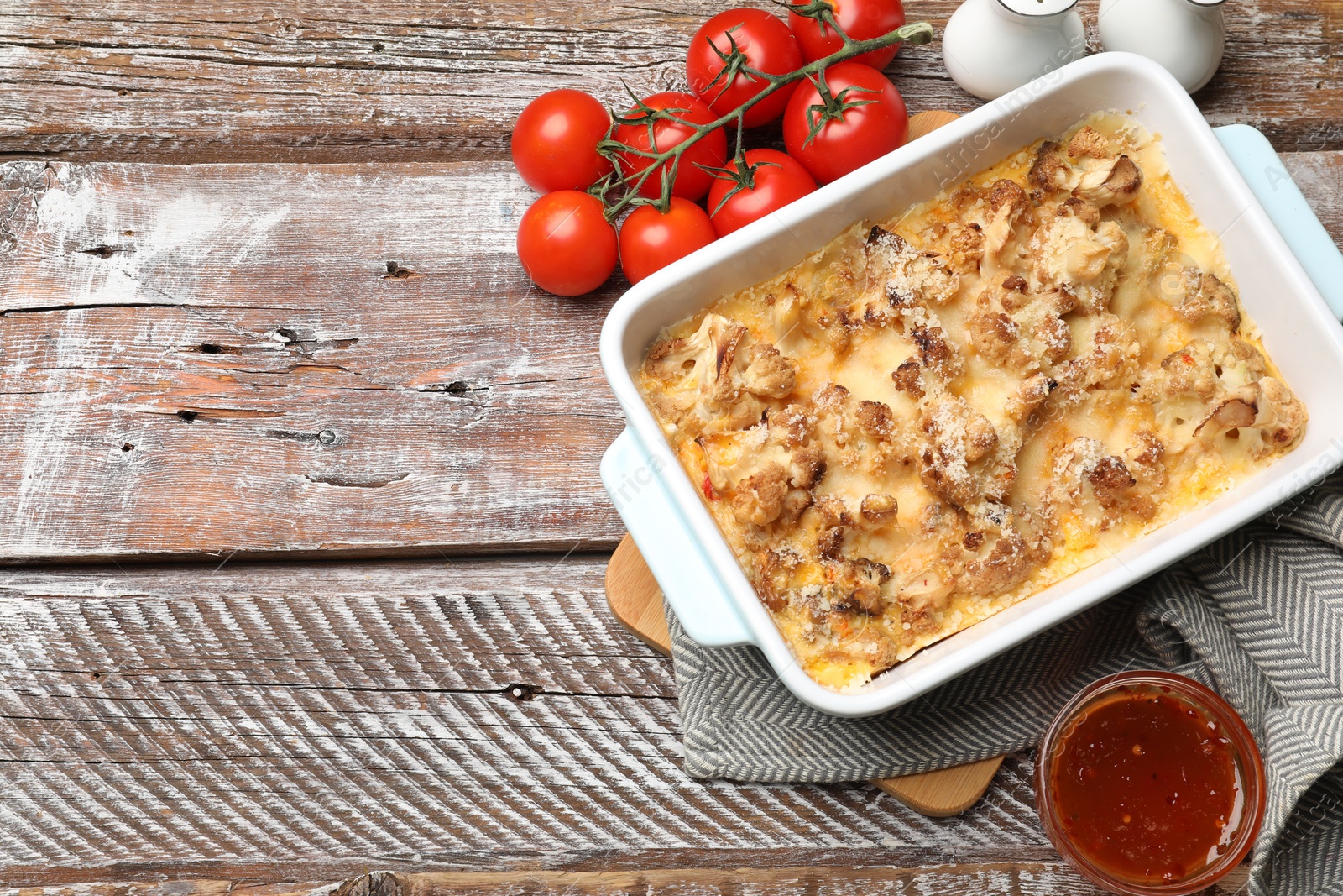 Photo of Tasty baked cauliflower, spices and tomato on wooden table, flat lay. Space for text