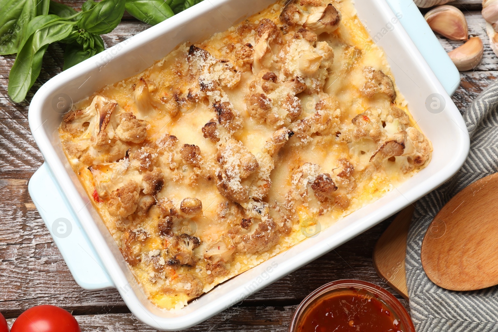 Photo of Tasty baked cauliflower, sauce and products on wooden table, flat lay