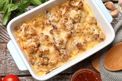 Photo of Tasty baked cauliflower, sauce and products on wooden table, flat lay