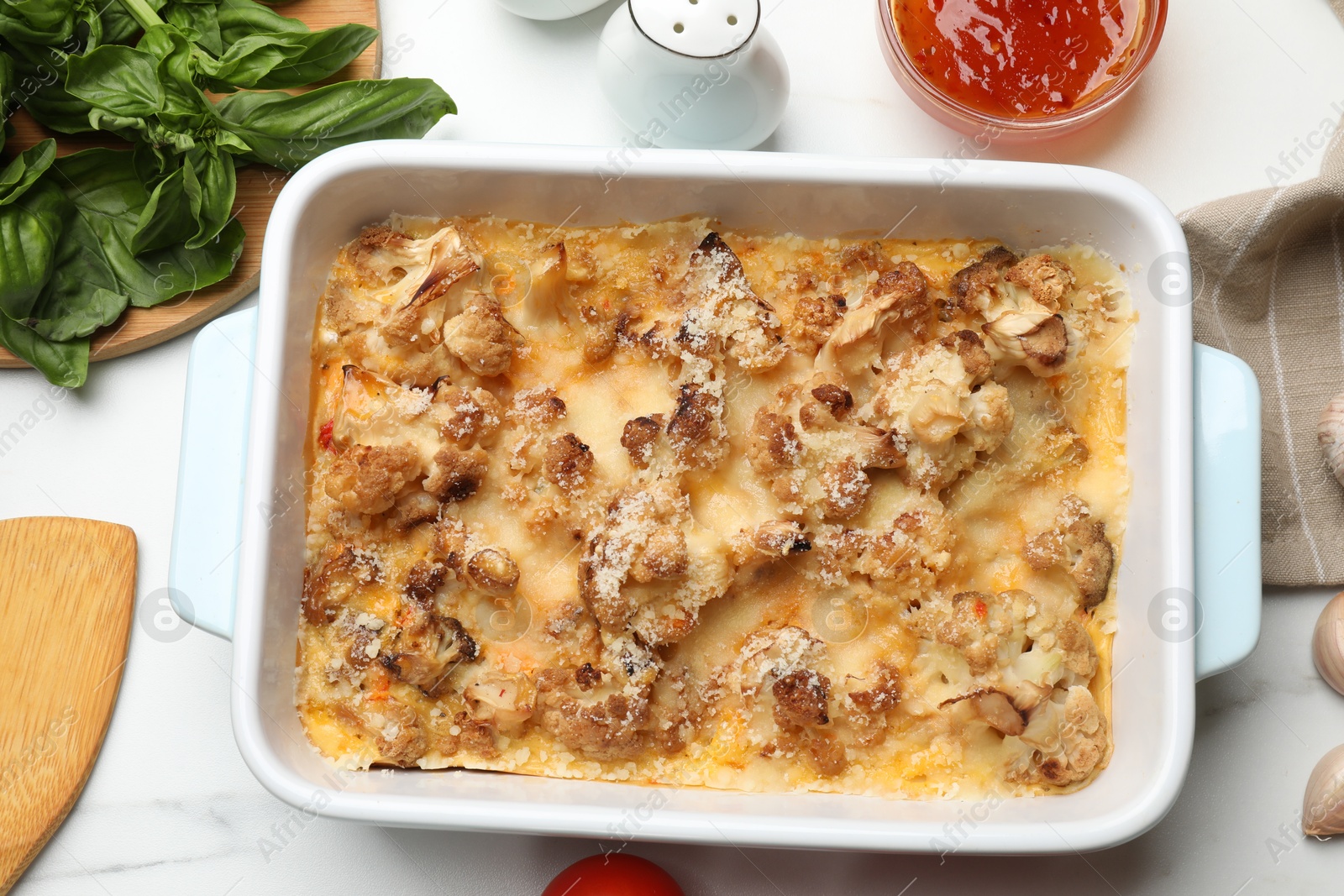 Photo of Tasty baked cauliflower, sauce, spices and basil on white marble table, flat lay